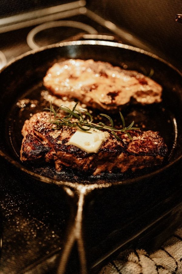 ローズマリーとバターをのせてフライパンで焼いている牛ステーキ