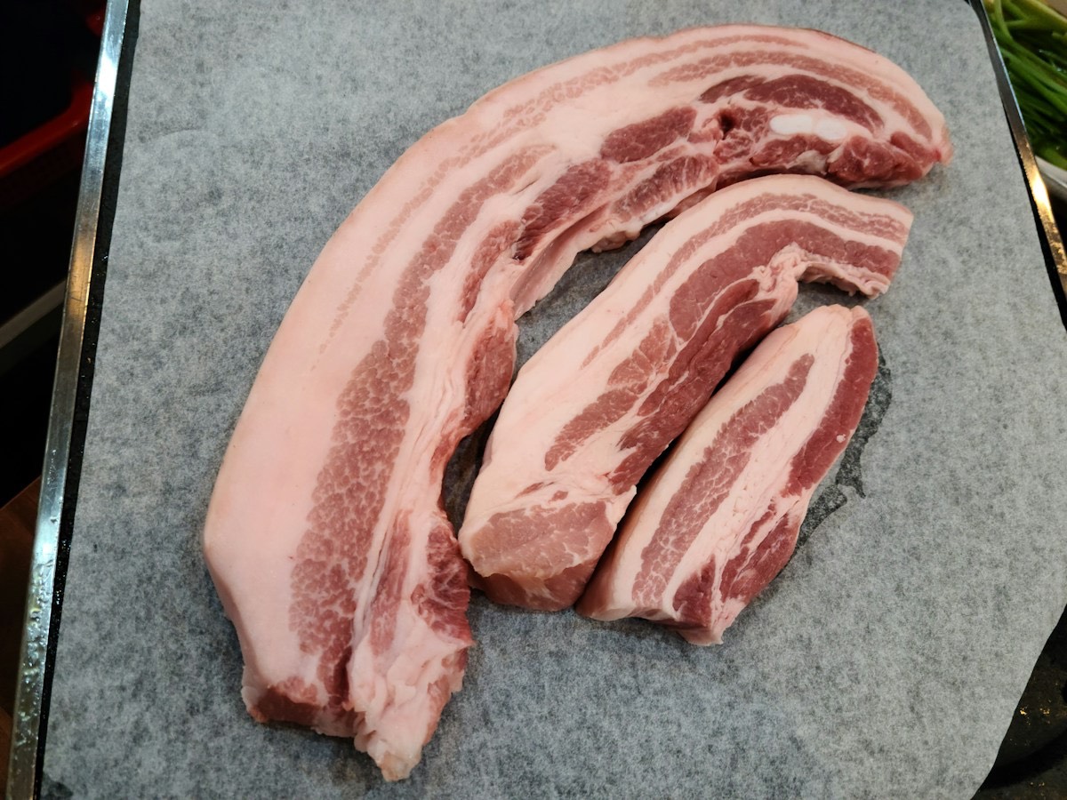 まな板の上に置いた生の豚バラ肉。赤身と脂がしま模様に重なっている